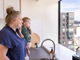 Woman holding a baby standing by the sink and looking out of the window above